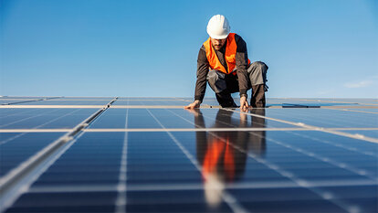 Ein Mann mit Schutzhelm und orangener Weste arbeitet auf einer Fläche mit Photovoltaikanlagen.