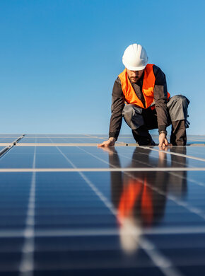 Ein Mann mit Schutzhelm und orangener Weste arbeitet auf einer Fläche mit Photovoltaikanlagen.